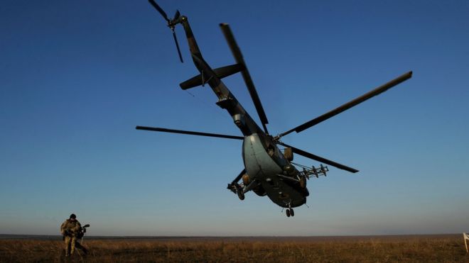 Военнослужащий идет возле украинского военного вертолета, летящего во время военных учений, на открытом зеленом поле с голубым небом