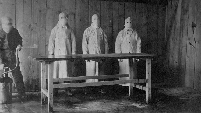 Tres hombres con batas y máscaras protectoras en el hospital de tratamiento de la peste en China, en 1910-11