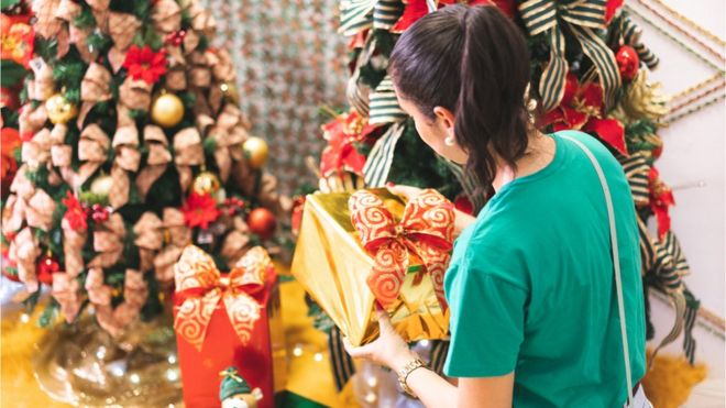 Mulher pegando presente de Natal em frente de decorações temáticas