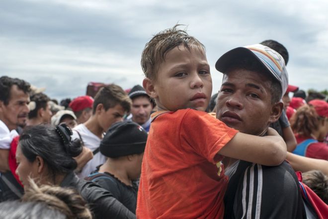 Мужчина несет ребенка на руках после того, как мексиканская полиция выпустила слезоточивый газ & gt;