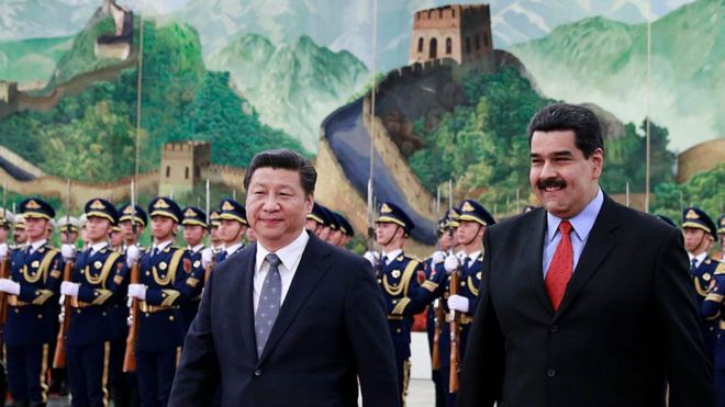 Xi Jinping e Maduro sorriem em cerimônia, aparecendo à frente de militares fardados e de uma grande pintura representando construções antigos em meio a paisagem chinesa