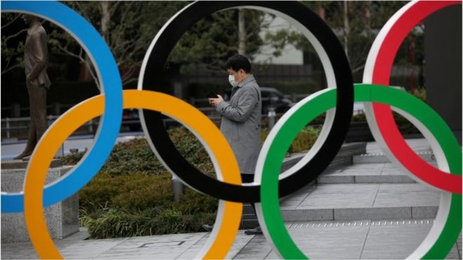 A man looks at his mobile phone next to The Olympic rings in front of the Japan Olympics Museum in Tokyo, Japan, March 4, 2020.