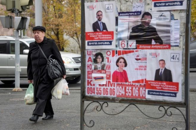 Люди проходят мимо предвыборных плакатов в Ереване 6 декабря 2018 года, за несколько дней до досрочных парламентских выборов 9 декабря