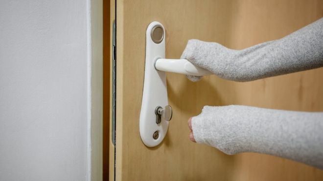 Una persona cogiendo una manija de la puerta con las mangas de su chompa.