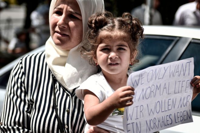Сирийская девушка держит плакат с надписью на английском и немецком языках «Мы хотим только нормальной жизни» возле посольства Германии в Афинах 19 июля 2017 года.