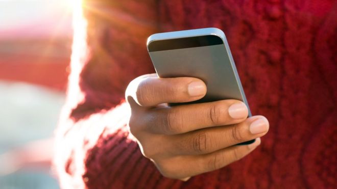 Feche acima da imagem da mão de uma jovem mulher que envia uma mensagem de texto em um smartphone.