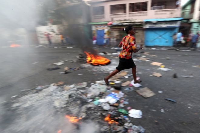 Женщина проходит мимо горящей баррикады во время антиправительственных акций протеста в Порт-о-Пренсе