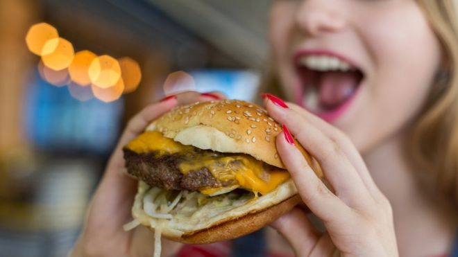 Mujer comiendo una hamburguesa.