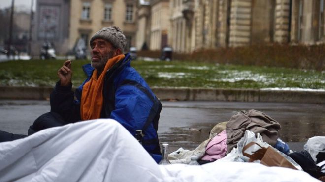 Бездомный мужчина сидит на асфальте с пуховым одеялом на одной из улиц Парижа, 1 марта 2018 года