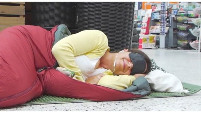 Woman sleeping on the supermarket floor wearing eye mask and earphones