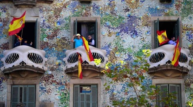 Люди машут испанскими флагами из Casa Batllo во время демонстрации за единство в Барселоне 29 октября 2017 года