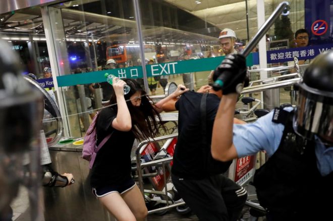 Полицейский Гонконга (С) падает назад, когда они дрались с протестующими за демократию