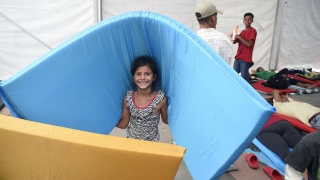 Девушка улыбается, когда она несет матрас в убежище на стадионе в Мехико