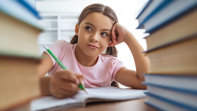 Una niña escribe entre libros.