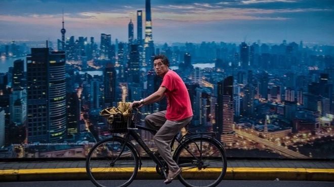 This picture taken on July 11, 2016 shows a man cycling past a billboard showing an aerial view of Shanghai