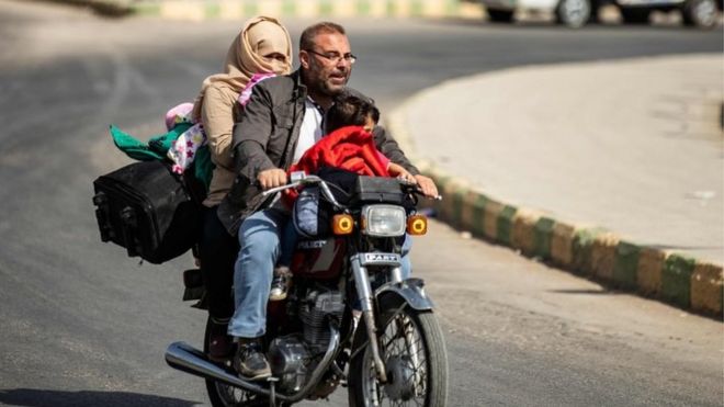 Displaced Syrians ride a motorcycle fleeing Turkey"s military assault on Tal Abyad on 11 October