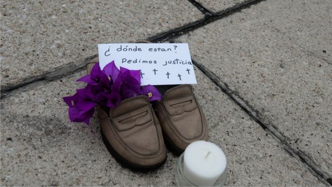 Пара туфель с цветами для девочек, сообщение «Где они? Мы просим справедливости »и свечи, поставленной родственниками пропавших людей на площади Эль-Ангел 10 июля 2011 года в Мехико