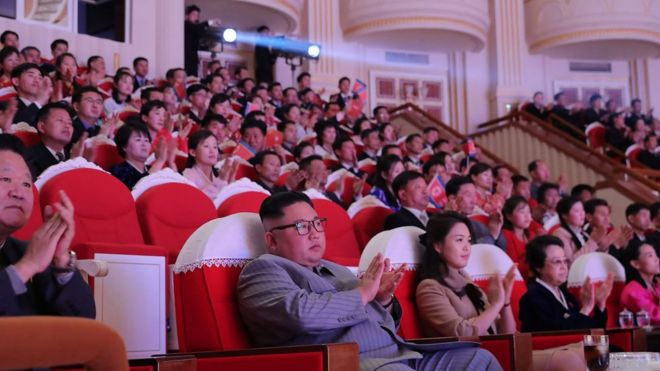 A crowded theatre claps at something out of view - but in the front row sits North Korean leader Kim Jong Un, but Kim Kyong Hui can be seen seated two places to his left