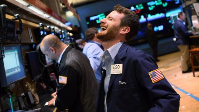 Imagem mostra homem sorrindo na bolsa de valores de Nova York