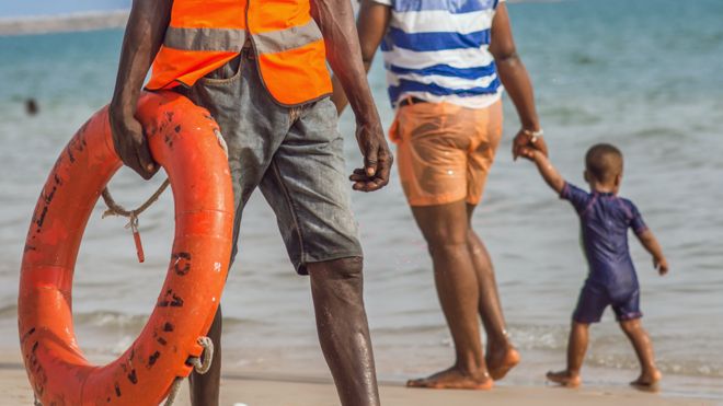 Спасатель и люди, прогуливающиеся по пляжу в Лагосе, Нигерия