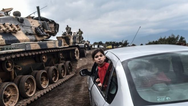 Турецкая девушка наклоняется из окна автомобиля, чтобы посмотреть, как танки и солдаты турецкой армии собираются вблизи сирийской границы в Хассе, в провинции Хатай 21 января 2018 года.