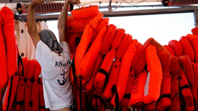 Член SOS-Mediterranee держит веревку, фиксирующую спасательные жилеты на Водолее, когда он плывет 22 июня 2018 года