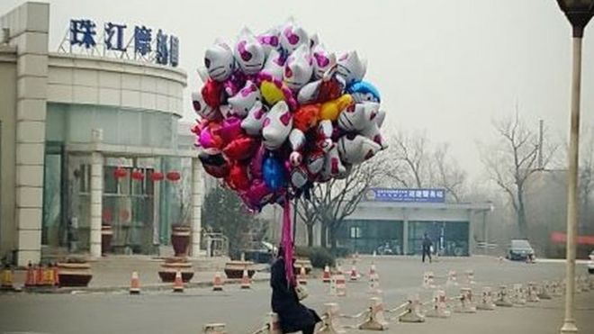 A man sits alone holding a bunch of balloons