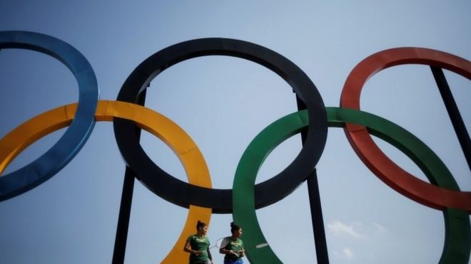 Brazilian badminton players Lohaynny Vicente (left), 20, and her sister Luana Vicente, 22, stand under a set of Olympic rings installed at Madureira Park in Rio de Janeiro (04 May 2016)