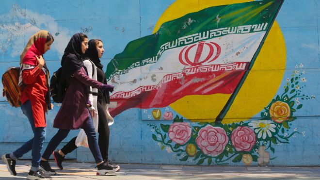 Young girls walk in front of a mural showing the Iranian national flag in the centre of the capital Tehran, on 23 April