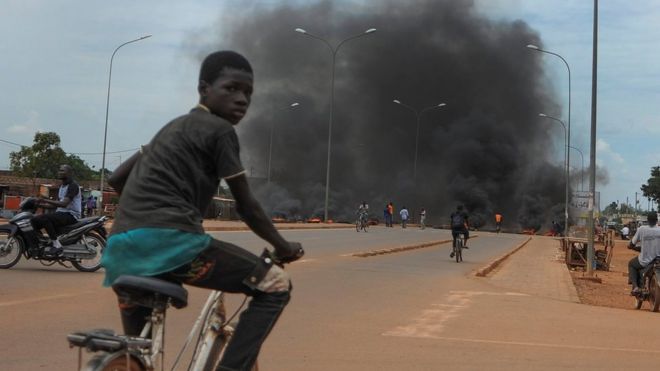 Ребенок ездит на велосипеде перед горящей баррикадой в столице Уагадугу