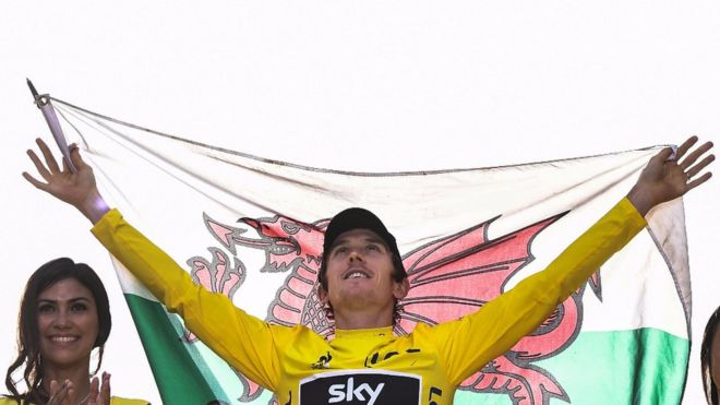 Герайн Томас держит валлийский флаг на подиуме победителя Тур де Франс