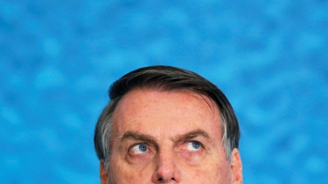 Bolsonaro olha para cima durante evento, com painel azul atrás