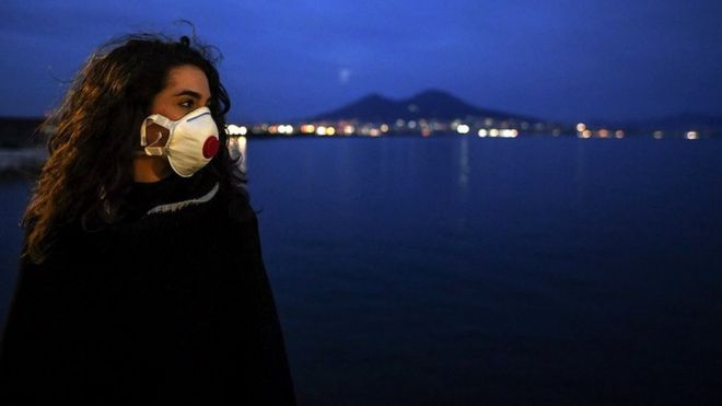 A woman wearing antivirus masks, to protect herself from the Coronavirus (Covid 19) waiting for a super moon walks at sunset on the Naples waterfront in front of the Vesuvius volcano.