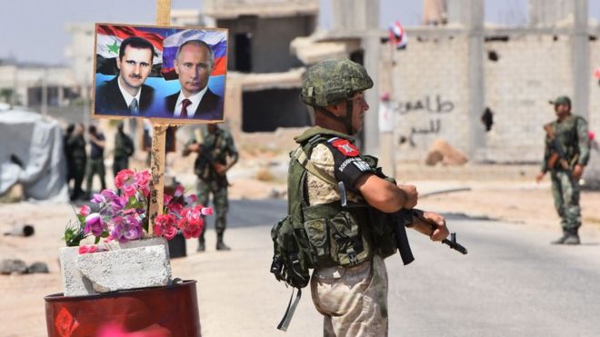Российские и сирийские правительственные силы стоят на страже возле плаката с изображением президента Сирии Башара Асада и президента России Владимира Путина на контрольно-пропускном пункте Абу-эль-Духур на восточной окраине провинции Идлиб (27 августа 2018 года)