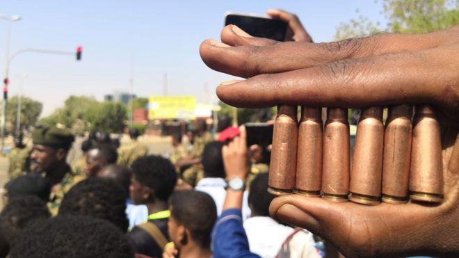 Суданский протестующий показывает патроны от пуль, когда другие собираются перед силами безопасности во время демонстрации в районе военного штаба в столице Хартум 8 апреля 2019 года.
