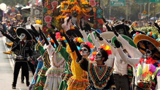 Люди, одетые в скелетный макияж, танцуют в красочном параде