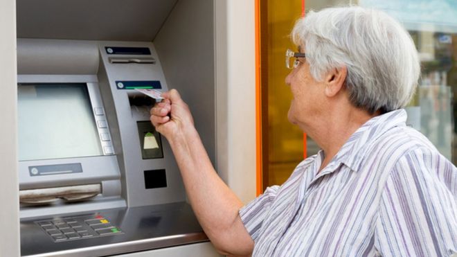 Пожилая женщина пользуется банкоматом