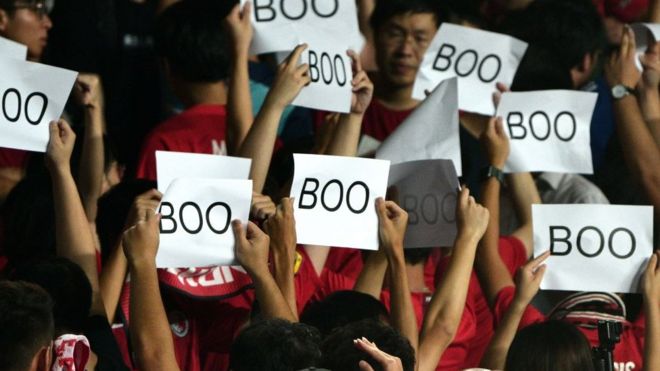 People turn their back and boo while holding up placards during the Chinese anthem at the start of the Qatar 2022 World Cup qualifying football match between Iran and Hong Kong