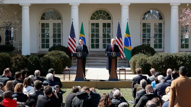 Bolsonaro e Trump no parlatório da Casa Branca, em foto de março, com bandeiras do Brasil e EUA atrás deles
