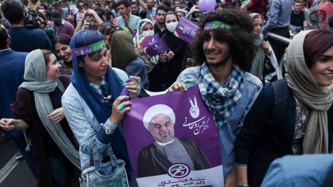 Сторонники недавно переизбранного президента Ирана Хасана Рухани держат плакат с его портретом, когда они выходят на улицы, чтобы отпраздновать его победу в центре Тегерана