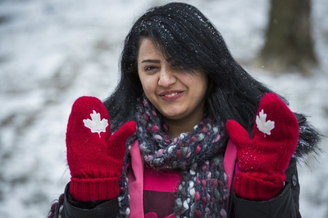 Сирийская беженка Рания Алхасан улыбается и поднимает свои канадские тематические варежки в Миссиссауга, Онтарио, Канада, четверг, 21 января 2016 года.