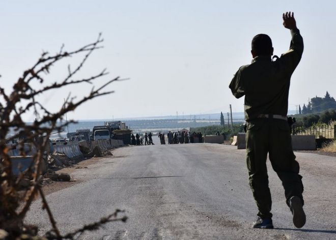Боец из Курдского Народного Подразделения Защиты (YPG) жестом указывает на перемещенных сирийцев, идущих к контрольно-пропускному пункту, контролируемому курдами, между удерживаемым повстанцами городом Азаз в северной части Сирии и городом Африн вдоль северной границы Сирии с Турцией, когда они пытаются пересечь границу. в июне 2017 года