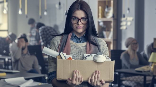 Mujer deja su trabajo con una caja en la mano.