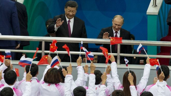 Президент России Владимир Путин и президент Китая Си Цзиньпин машут зрителям во время товарищеского матча между сборными командами Китая и России по хоккею с шайбой 8 июня 2018 года в Тяньцзине, Китай
