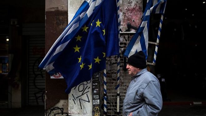 Человек идет мимо флагов Греции и ЕС