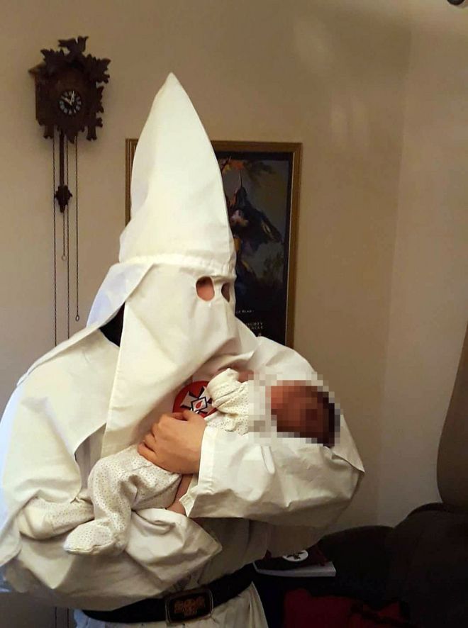 Мужчина в белом костюме KKK с ребенком на руках
