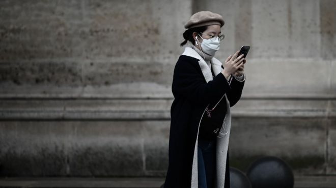 Woman in a mask check her phone, Paris, 31 January 2020