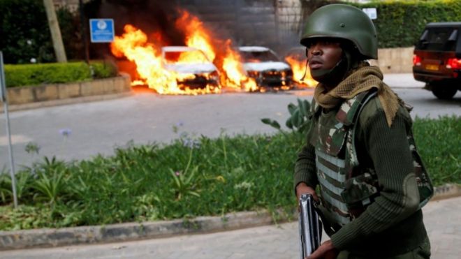 Милиционер проезжает мимо горящих автомобилей на месте, где 15 января 2019 года в гостиничном комплексе Дусит, Кения, были слышны взрывы и выстрелы.