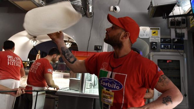 A pizza-maker prepares a pizza in Naples