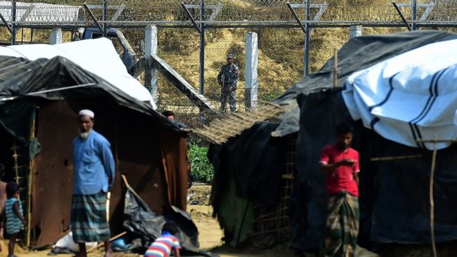 Сотрудники службы безопасности Мьянмы следят за границей Мьянма-Бангладеш, когда 1 марта 2018 года беженцы рохинджа стоят возле своих временных укрытий возле Томбру в бангладешском районе Бандарбан.